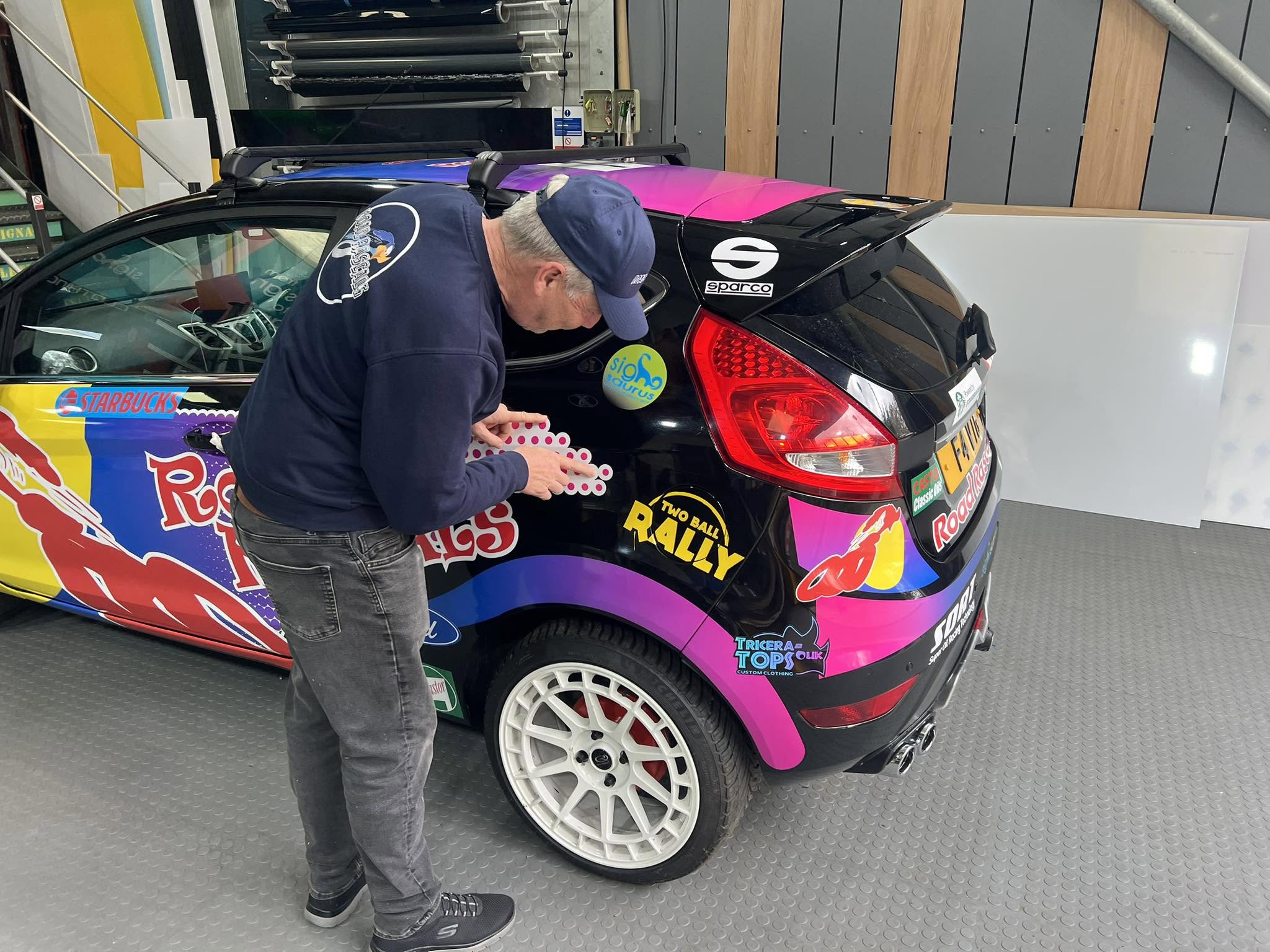 Applying the Road Rascals decal wrap to the rally Fiesta in the workshop