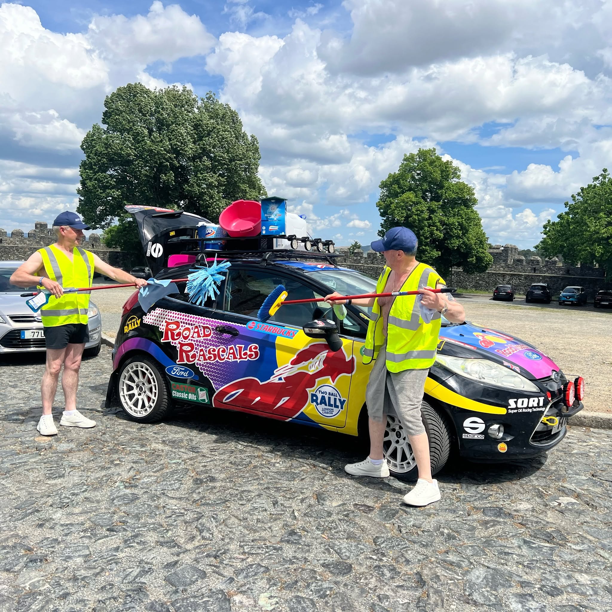 Peter and Nigel in hi-vis vests washing the rally car outside a castle